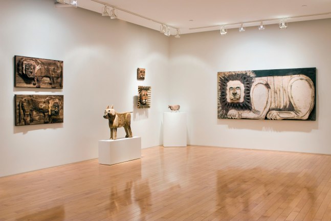 Photograph showing a corner view of an exhibition space, with five sculptures hanging on the walls and two sculptures on pedestals