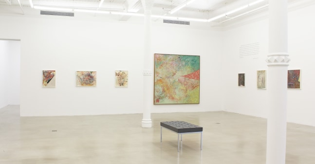 Photograph showing a corner view of an exhibition space, with seven paintings hanging on white walls