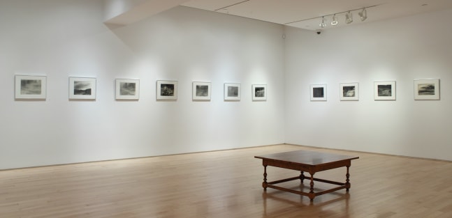 Photograph showing a corner view of an exhibition space, with eleven framed drawings hanging on white walls