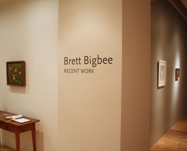 Photograph showing a view of an exhibition, with three framed works hanging on the walls and wall text that reads &quot;Brett Bigbee: Recent Work&quot; on the wall in the center