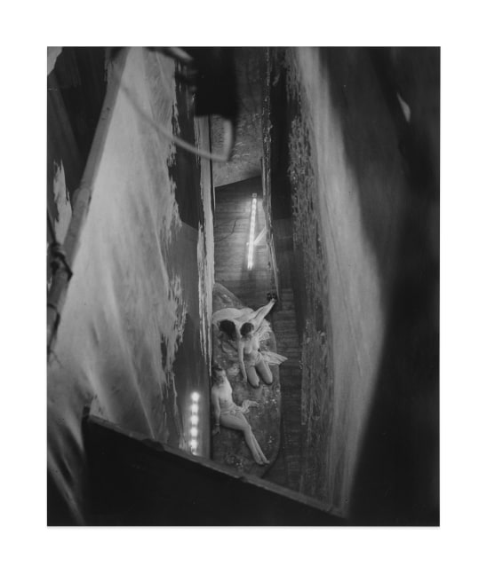 Black and white gelatin silver print depicting a birds eye view of three angelic naked women on stage.