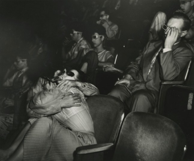 A black and white photographic print by Weegee depicting two people aggressively kissing in the seats at the Palace Theatre