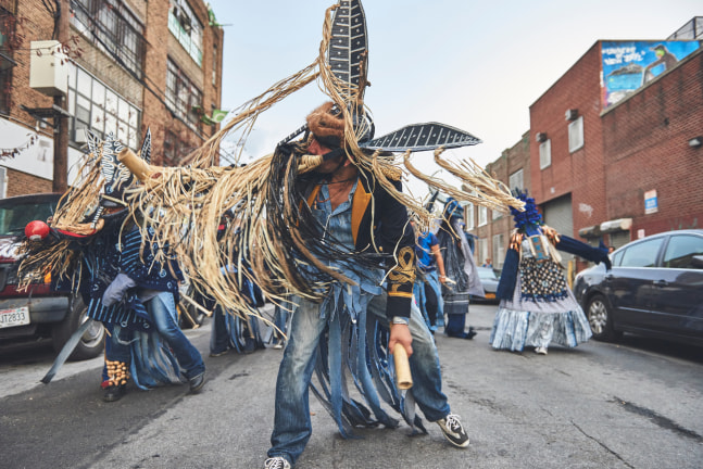 Men in indigo costumes dance down a city street.