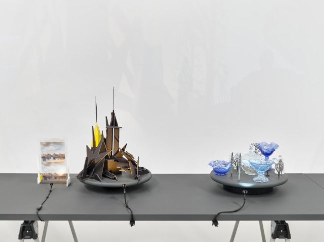 A series of assemblage sculptures comprised of upside down crystal vases, miniature street lamps, photographs printed on plexiglass and steeples made from styrene atop rotating platforms.