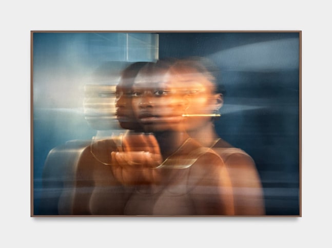 A photo by Kenturah Davis mounted on lenticular glass of a woman in gold jewelry reflected against a blue wall.