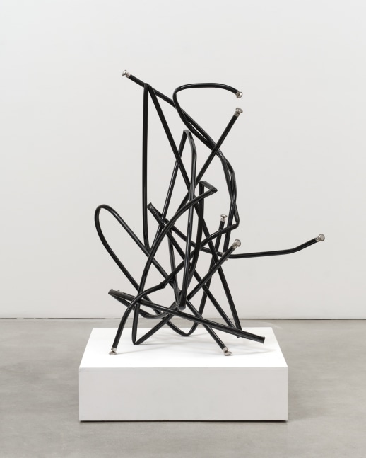 A freestanding sculpture by Josh Callaghan of black metal tubing with chair leg caps entangled and extending in all directions.