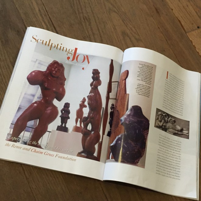 Magazine spread out on a dark wood table. It features a photo of the first floor of the Chaim Gross Studio with large humanesque wood sculptures in a spacious white room. 