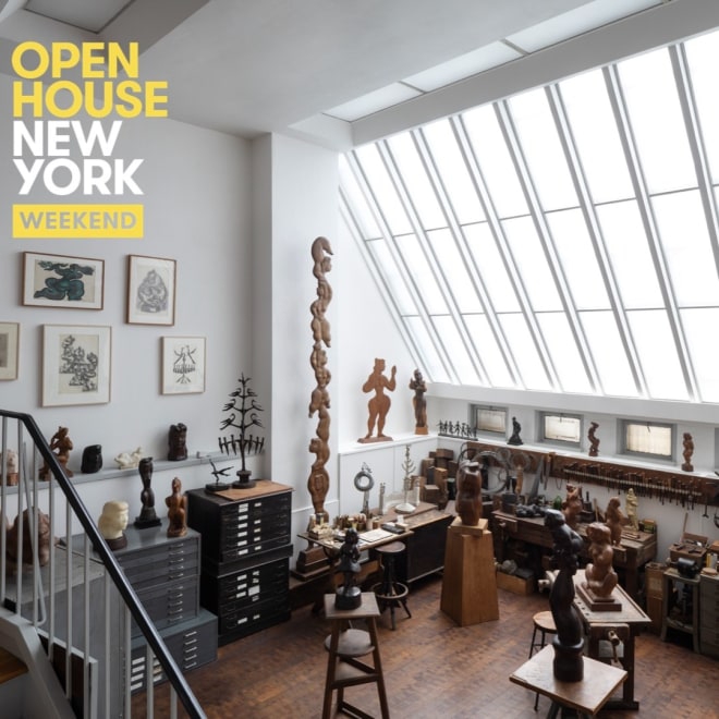 Photograph of a studio space. There is a large skylight taking up a quarter of the right side of the image. There are sculptures around the middle of the floor on pedestals. There are drawings on the walls and tools located under the skylight. Text says, "Open House New York Weekend" on the top left corner. 