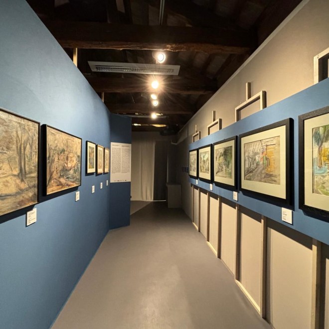 Framed horizontal landscape artworks line a hallway with blue walls and a gray floor.