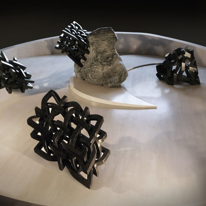a sculpture by Elizabeth Turk of four cubes made of interlaced black marble arranged in a dry riverbed
