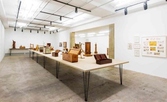 A tabletop full of H.C. Westermann&rsquo;s implements, including boxes (in foreground). At right, drawings and prints.