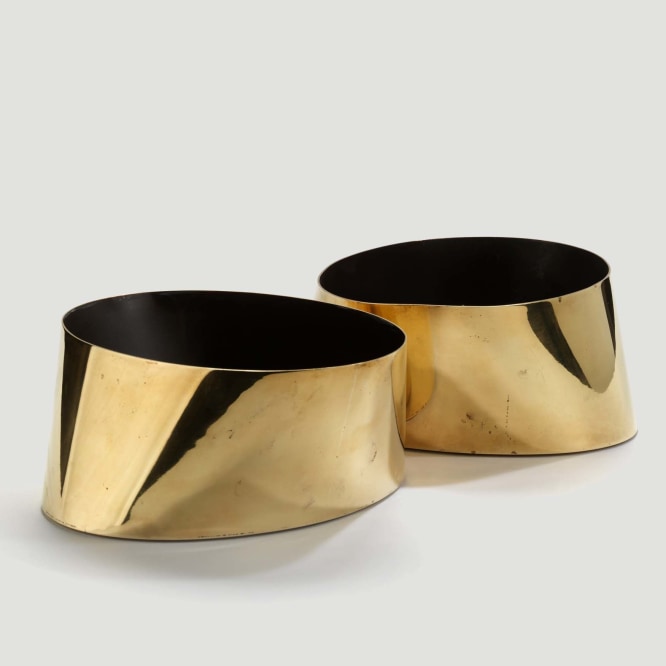 photograph of two circular gold vases with black interiors in a blank room 