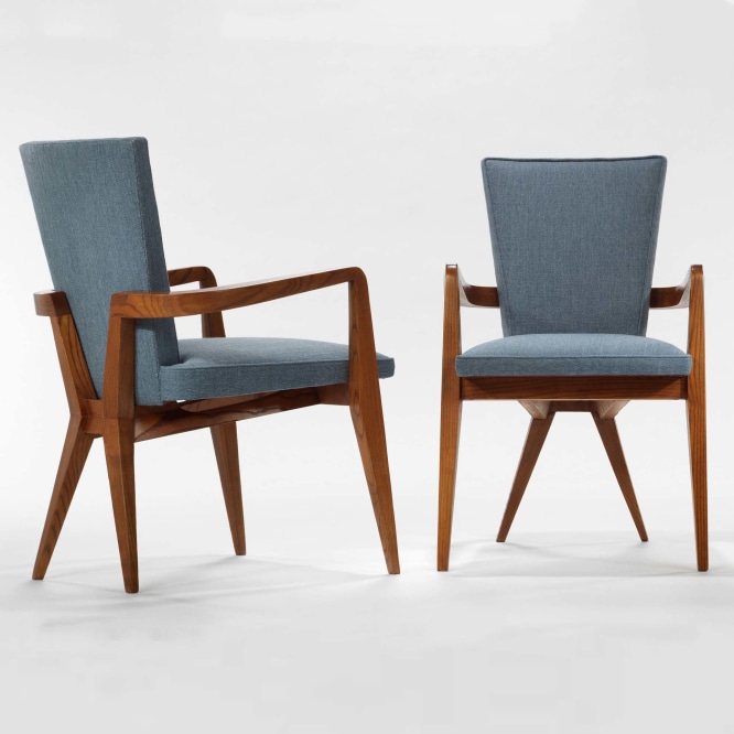 photograph of 2 chairs in a blank room, chairs have wooden legs and blue upholstery 