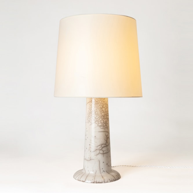 Table lamp made using raku white glaze and adding a fabric shade, with footed base in the ceramic. 