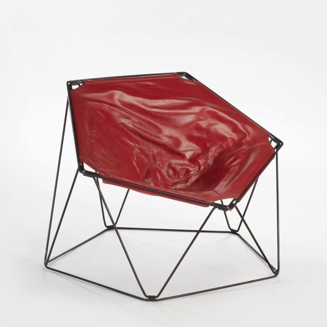 photograph in a blank room of pentagonal shaped chair by Barray with red leather upholstery and black metal wire legs