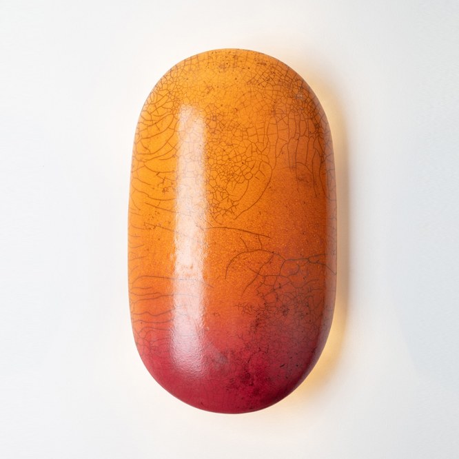 Raku glaze orange and red crackle effect on a pill shaped wall sconce. light turned on in image. 