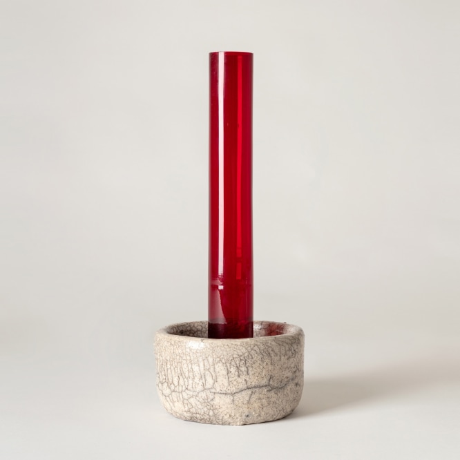 Red glass tubular vase sitting inside raku ceramic holder. 