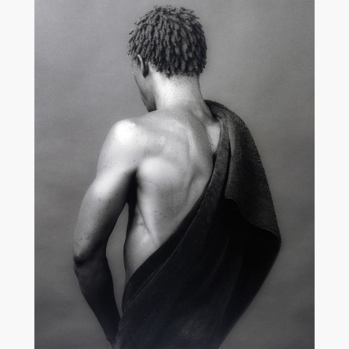 Shirtless man turned away from the camera with a fabric draped over his right shoulder.