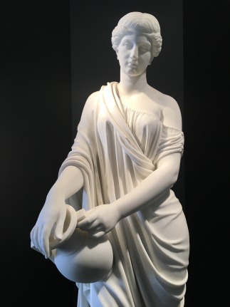 Image of a white marble sculpture by William Henry Rinehart depicting the Woman of Samaria in a draped garment, holding a water jug.
