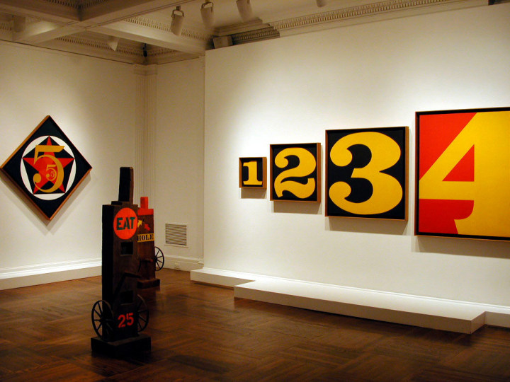 Installation view of Robert Indiana: Letters, Words and Numbers at C&M Arts featuring the paintings The Small Diamond Demuth Five and Exploding Numbers, and the herms Eat and Hole.