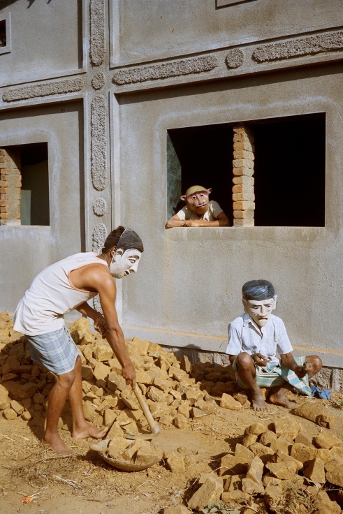 Archival pigment print featuring three people laboring in paper Mache masks