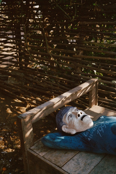 Archival pigment print featuring one person in paper Mache mask lying on a bench