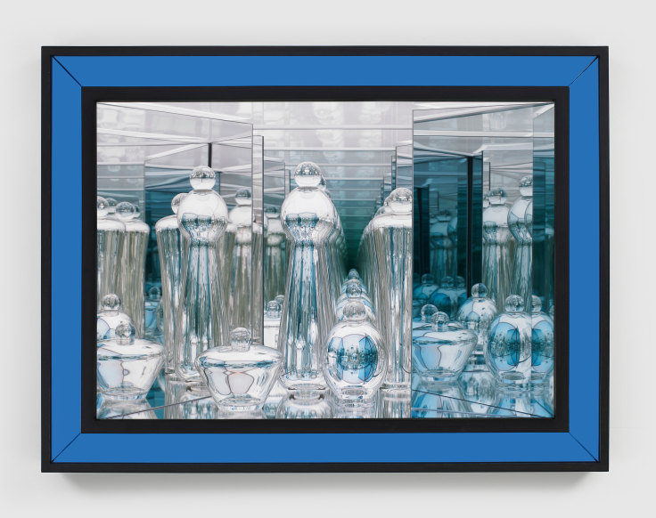 Handblown glass sculptures with reflective surfaces in a lit space framed behind a blue dyed walnut frame