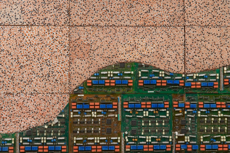 half of the image is composed of swirling orange electrical wires while the other is a mostly green surface of other types of electrical components