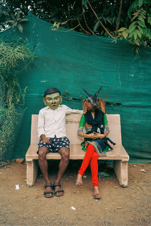 Archival pigment print featuring two people seated on a bench in paper Mache masks
