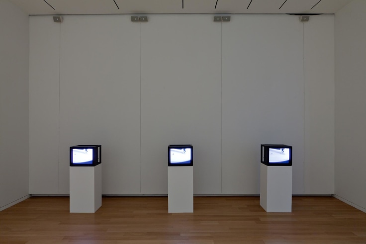 three TV screens, each one placed on top of a white pedestal