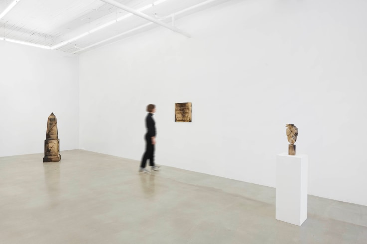 person walking in between three wooden sculptures
