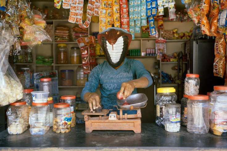 Archival pigment print featuring one person in snake paper Mache mask weighing produce