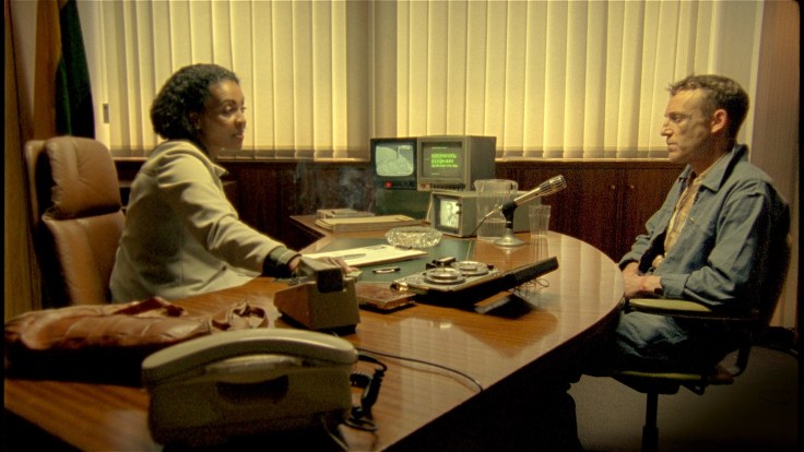 video still of two individuals seated in a closed office.
