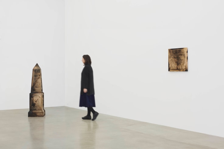person walking through the the gallery between two wooden sculptures