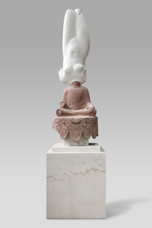 A bronze sculpture atop a rectangular base, with the bottom half resembling a sitting buddha and the top half resembling the body of a nude female figure with missing limbs