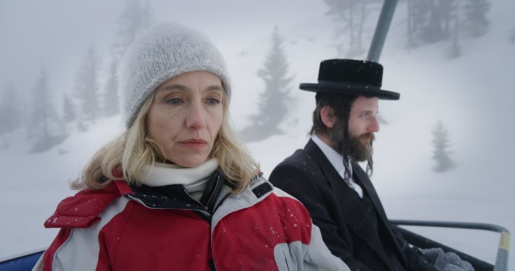 Video still of two people, one clothed in contemporary winter garments and the other in traditional Hasidic clothes, sitting on a ski lift.