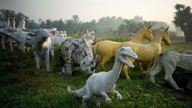 statues of a white dinosaur, a rhino, two bulls and other animals facing different directions