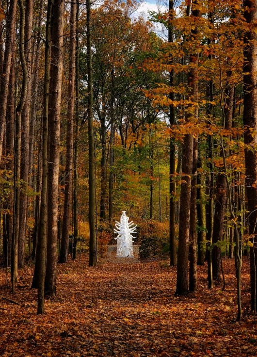 A white marble sculpture of an anthropomorphic from in the woods during Fall
