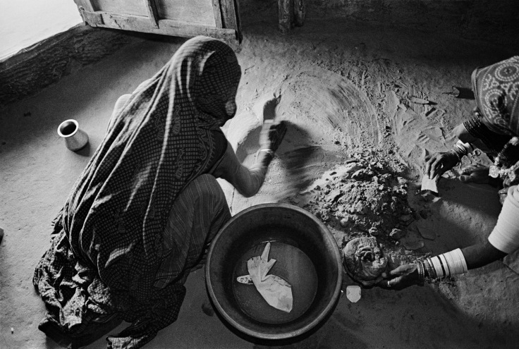 grayscale photograph of a woman wearing a veil, kneeling and collecting dirt