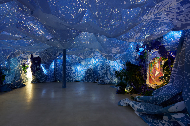 Installation including two paintings, blue wall and indigo ceiling hangings, and tropical foliage by Firelei B&aacute;ez.