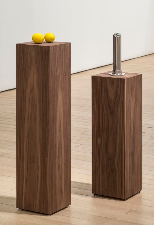 installation view of two pedestals, one with a metal object and the other holding two lemons