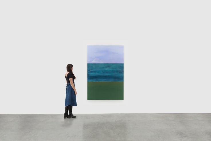 A woman views a three sectioned abstract painting depicting the sky, the ocean and a yellowish green block of color