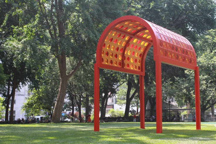 Red painted wood and steel prismatic glass structure set up on grass in a park