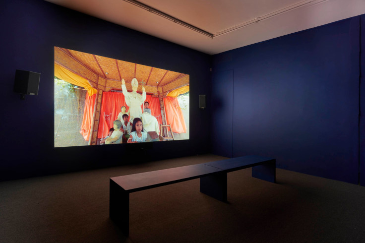 a dark room with a video projection showing children with the statue of a pope