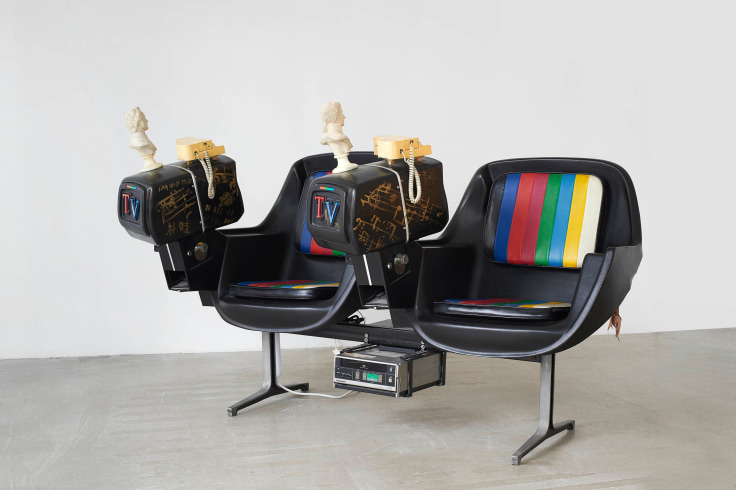 Two chairs attached to one another, each with their own small television monitor