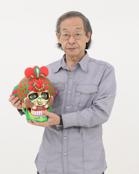 Portrait of artist Keiichi Tanaami holding one of his brightly colored sculptures that looks like a skull