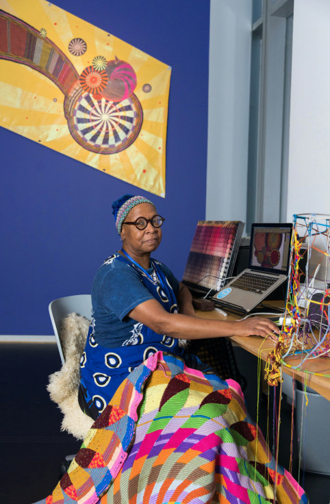 Xenobia Bailey in her studio, with part of &ldquo;Mothership Sail,&rdquo; crochet mandala image printed on canvas and hand-painted adornment, in the background
