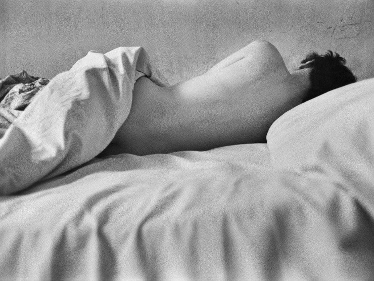 A naked woman is photographed from behind, exposing her back, as she sleeps