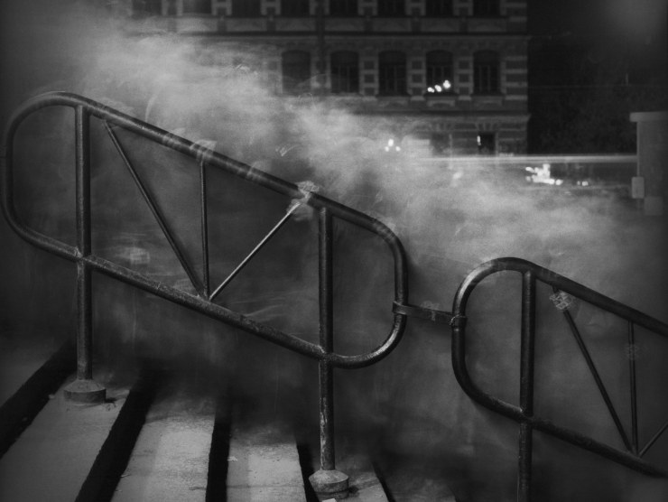 A time-lapse image of blurry figures going up a staircase at night in a black and white photo