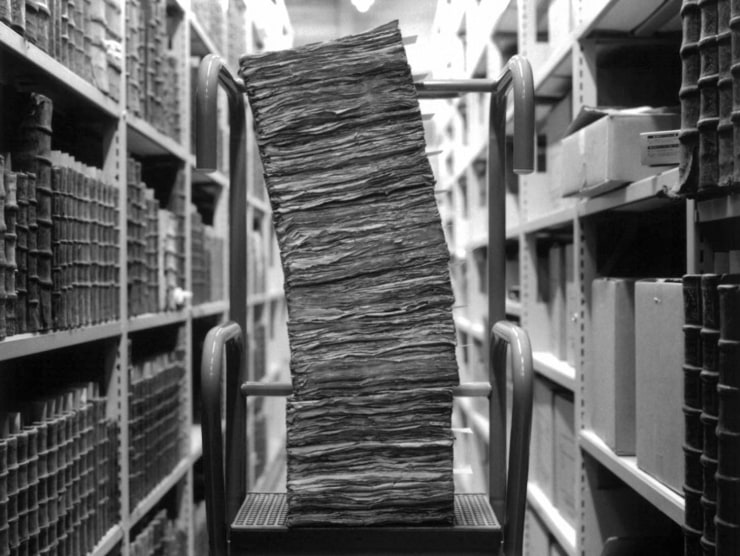 A stack of leaning papers in a library aisle, photographed in black and white